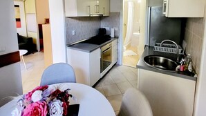 A compact kitchen with white cabinets, a stainless steel sink, and a dining area with a table set for two. - Green Terrace Apartment I (Dubrovnik)