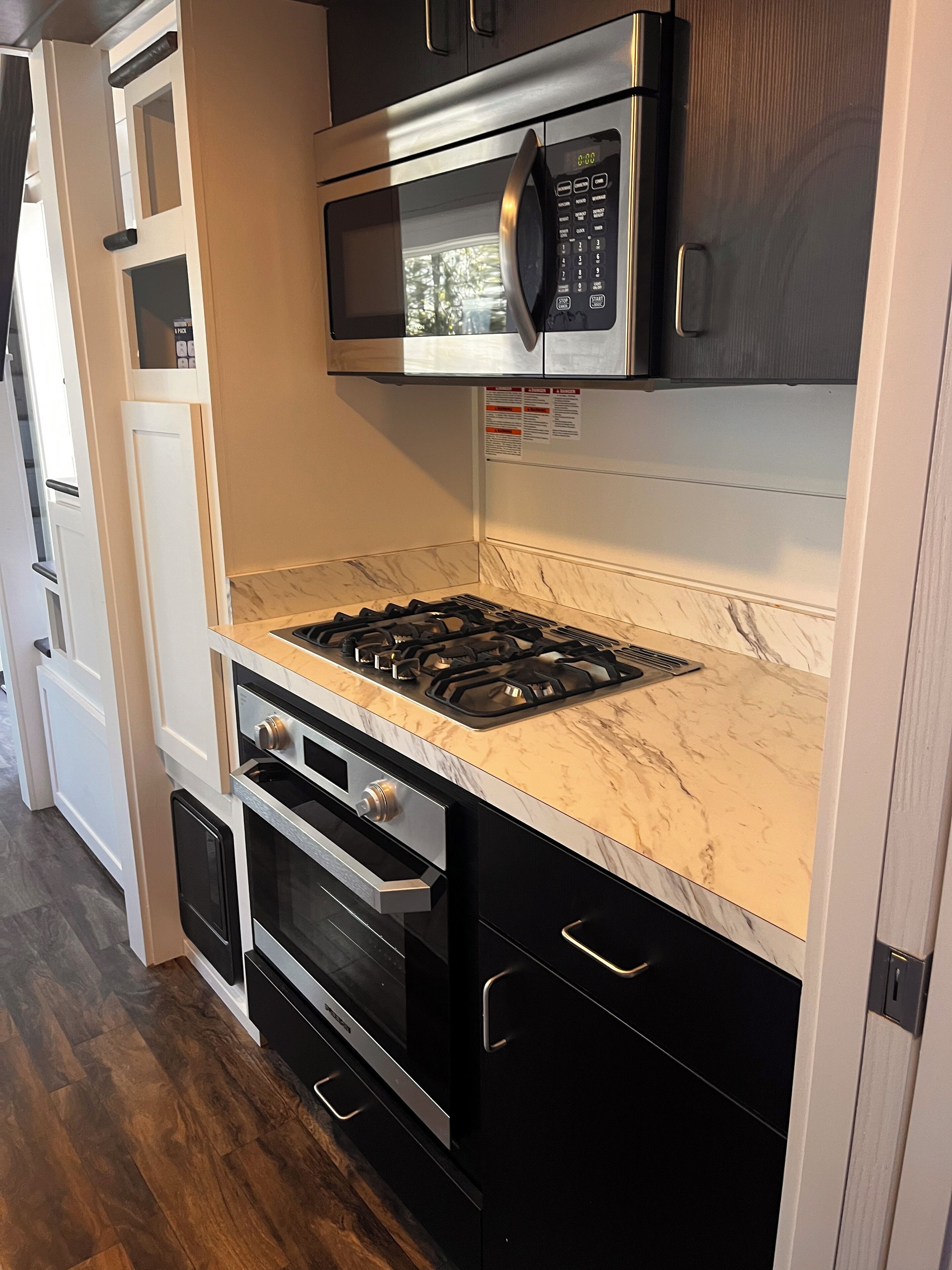 A compact kitchen with a built-in microwave, gas stove, oven, and a marble countertop.
