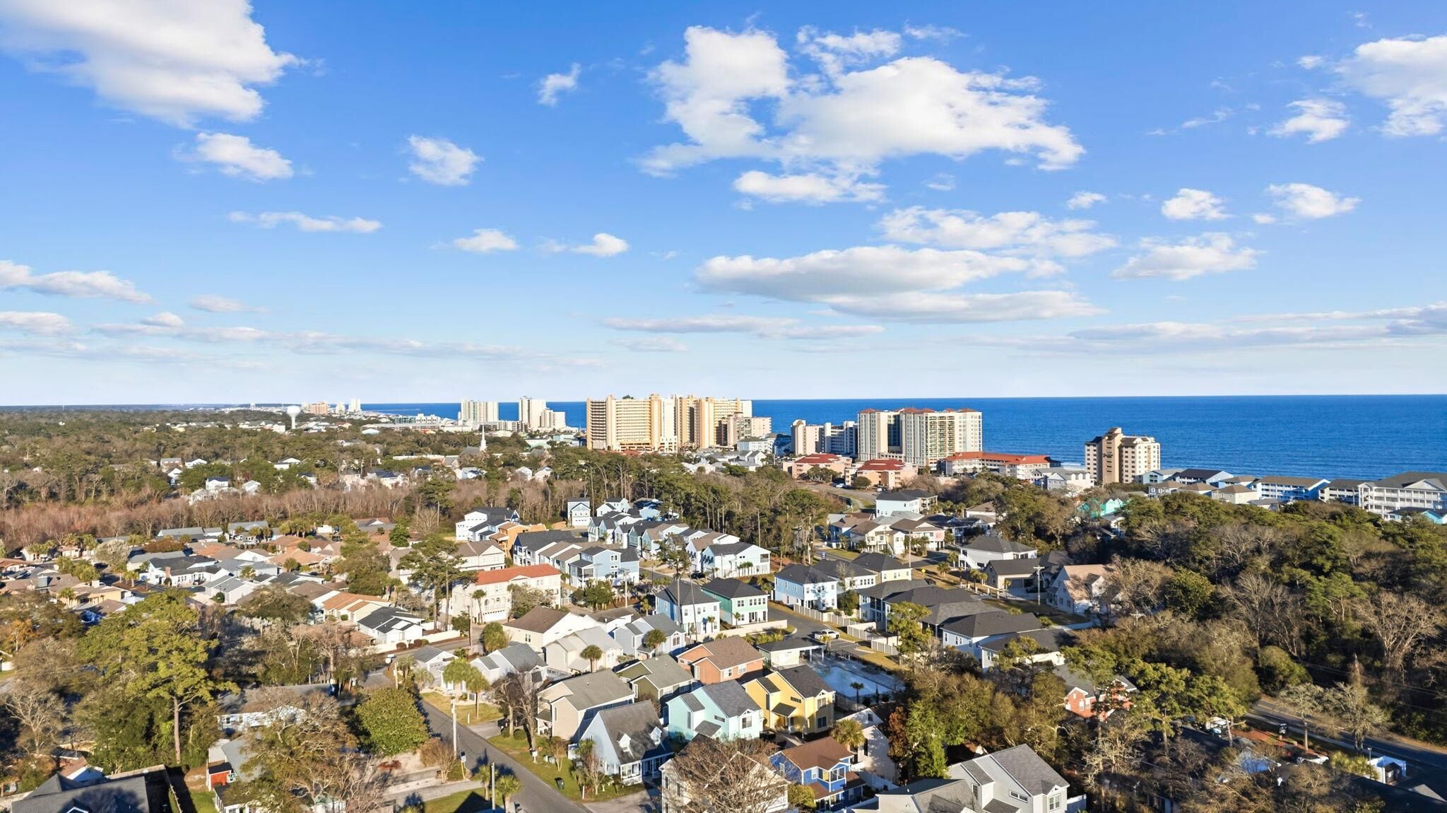 A coastal residential area with houses, a beachfront, and high-rise buildings in the background.
