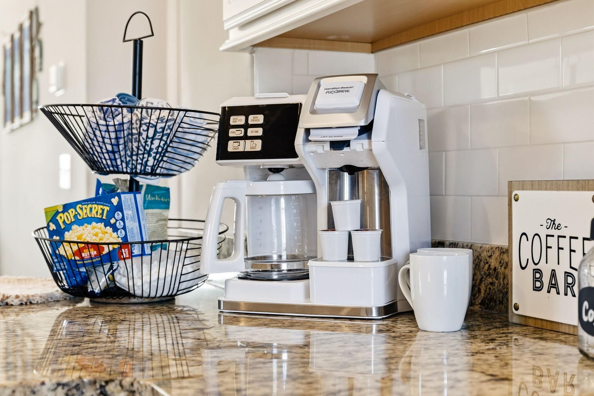 A kitchen with a coffee maker, a popcorn container, and a coffee bar sign.