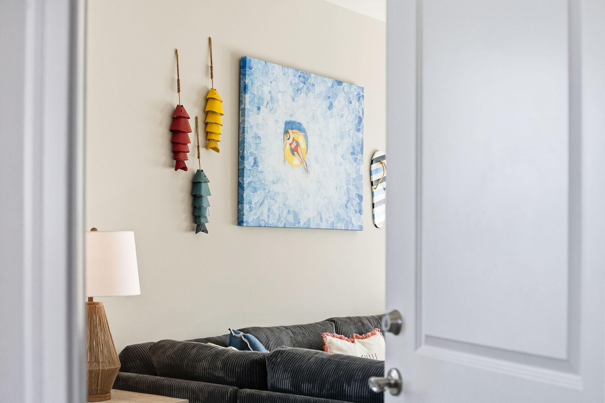 Une pièce avec un canapé de couleur sombre, un tableau accroché au mur et un objet décoratif suspendu.