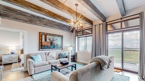 A spacious living room with a large window, a ceiling with exposed beams, and a modern chandelier. - Wilderness retreat with pool, hot tub, and sauna access - wood-burning fireplace (Sugar Mountain)