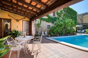 Une terrasse extérieure avec une piscine, des chaises en métal blanc et des plantes en pot.