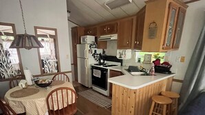 Eine kompakte Küche mit Essbereich, Holzschränken, einem Kühlschrank und einer kleinen Kücheninsel mit Barhocker.