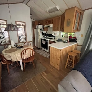 A compact kitchen with a dining area, wooden cabinets, a refrigerator, and a small island with stools.