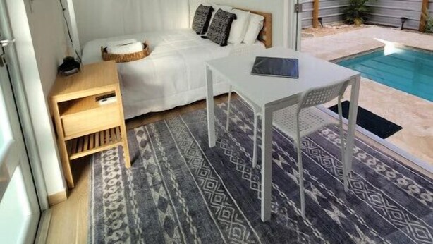 Habitación compacta con cama, una mesita, televisión y zona de piscina con pérgola.