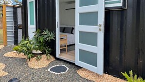 Edificio metálico negro compacto con puerta y ventanas blancas. En su interior, hay una cama y una mesita.