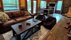 Un interior de cabaña acogedor con techo de madera, un sofá de cuero, una mesa de centro y un comedor con mesa y sillas de madera.
