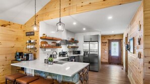 Una cocina moderna con paredes de madera, una isla central con taburetes, un letrero de cafetería y electrodomésticos de acero inoxidable.