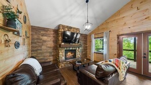 Una sala de estar acogedora con chimenea de piedra, sofás de cuero y un televisor.