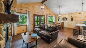 Un interior cálido de cabaña con revestimiento de madera, un sofá de cuero, una mesa de comedor y una pared de piedra.
