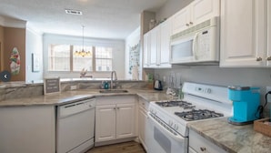 A kitchen with white cabinets, a gas stove, a microwave, and a coffee maker.