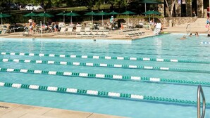 Ein Schwimmbecken mit mehreren Bahnen, Liegestühlen und Sonnenschirmen.