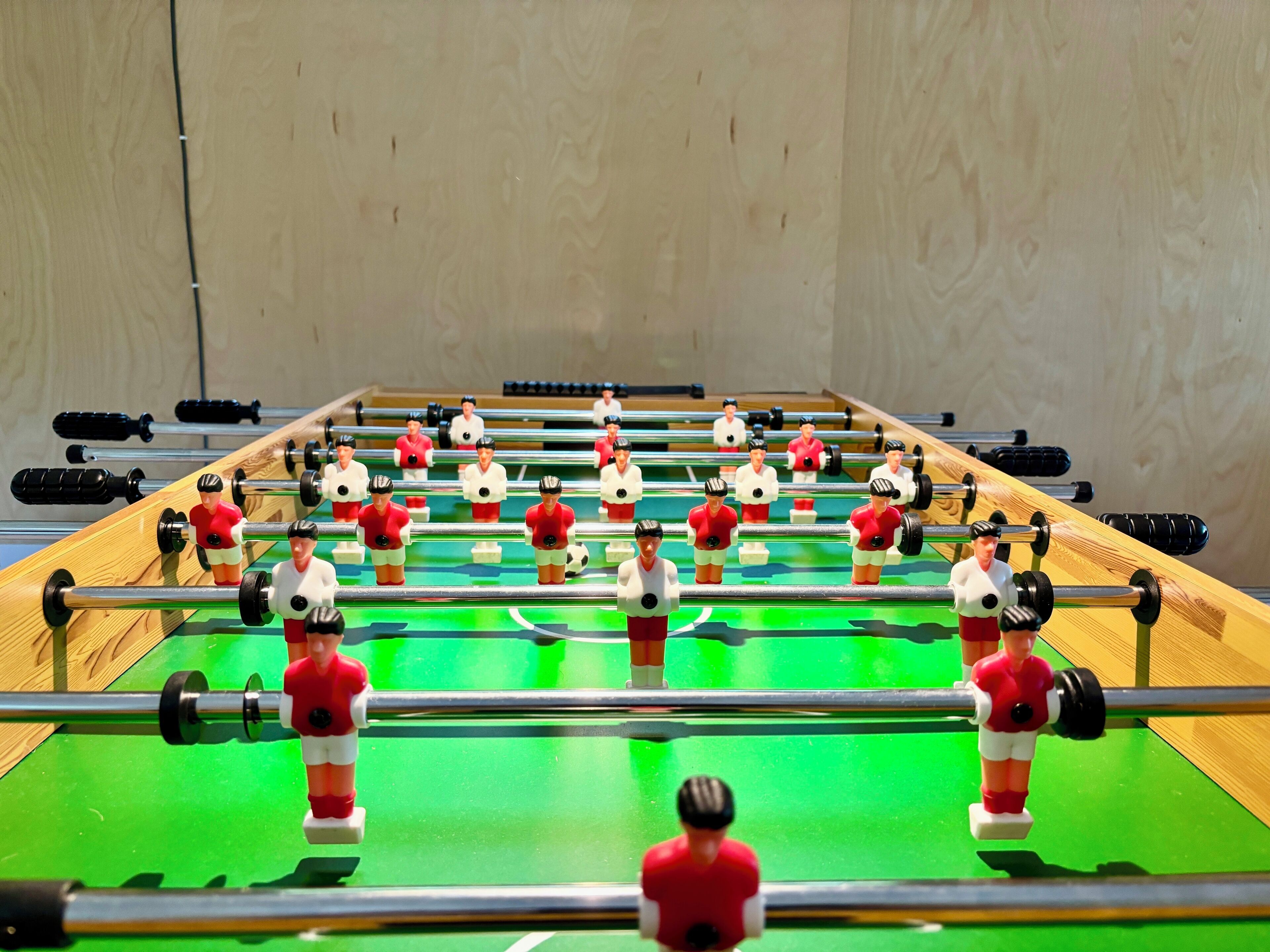 A foosball table with two teams of players, one in red and one in white, set against a wooden wall.