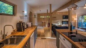 A modern kitchen with a wooden countertop, stainless steel sink, and a built-in stove. There is a seating area with a sofa and a TV. - Scandinavian HideOut for Couples and Families, Firepit, Outdoor Games (Sevierville)