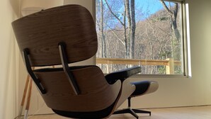 A modern chair with a wooden backrest and black armrests, positioned in a room with a large window offering a view of trees. - Scandinavian HideOut for Couples and Families, Firepit, Outdoor Games (Sevierville)