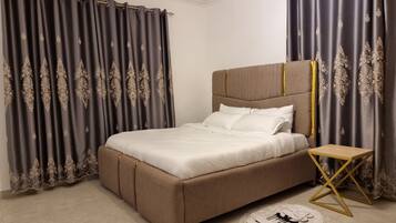 A bedroom with a large bed, curtains, a bedside table, and a small rug.