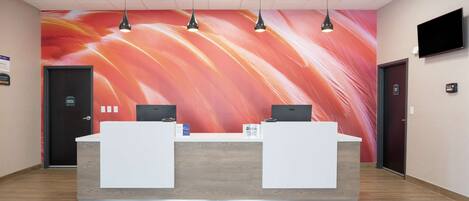 A reception desk with two computers, a large abstract mural, and a flat-screen TV on the wall.