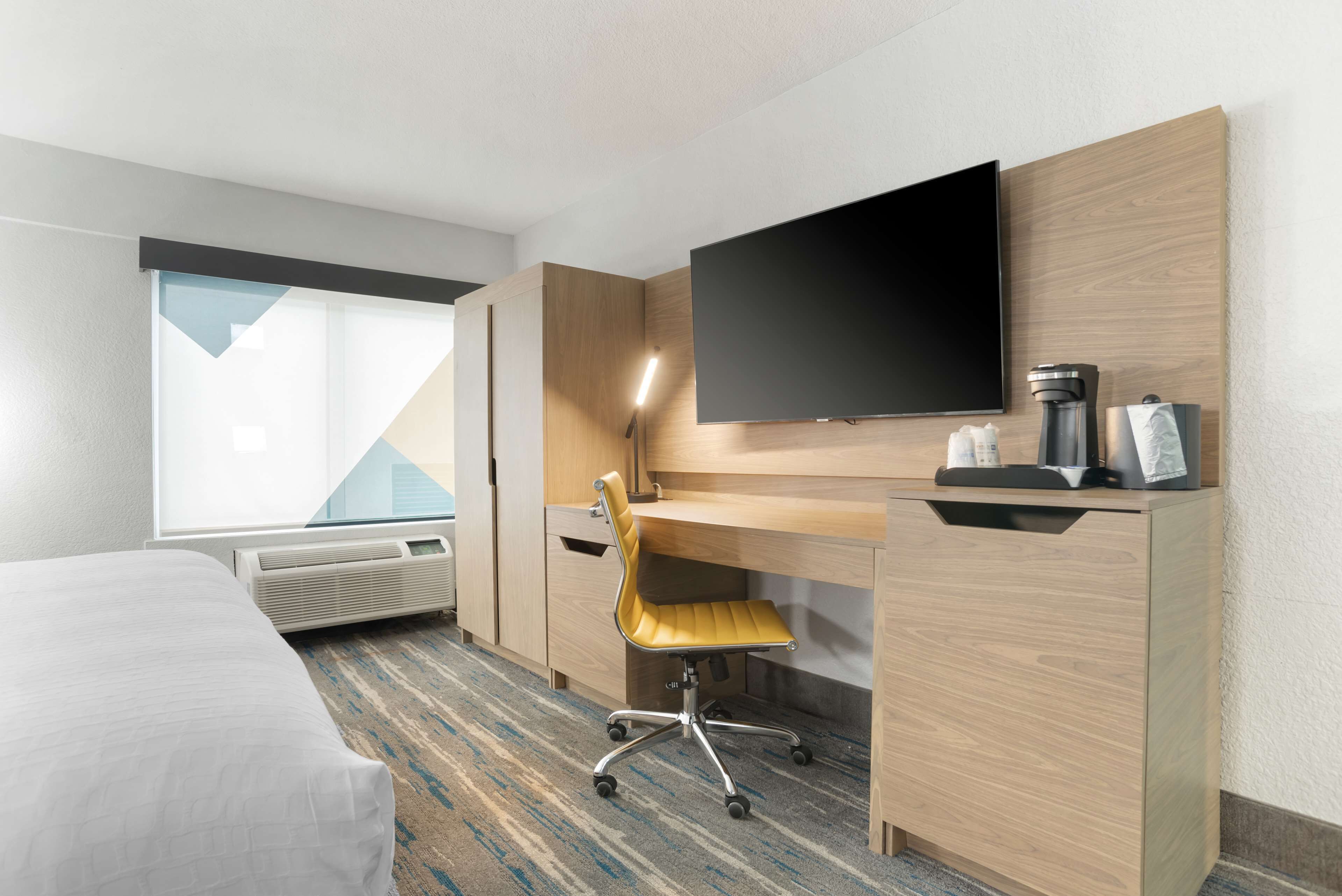 A hotel room with a bed, a desk with a chair, a flat-screen TV, a coffee maker, and a window with a view.