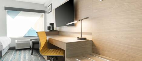 Une chambre d’hôtel moderne avec un bureau en bois, un téléviseur à écran plat fixé au mur, un fauteuil jaune confortable et un lit donnant sur les montagnes.