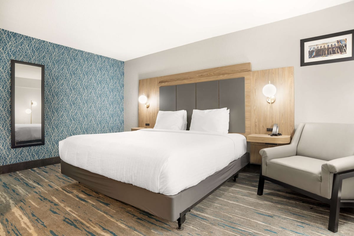 Una habitación de hotel con una cama grande, una silla, una mesita de noche y una lámpara de pared.