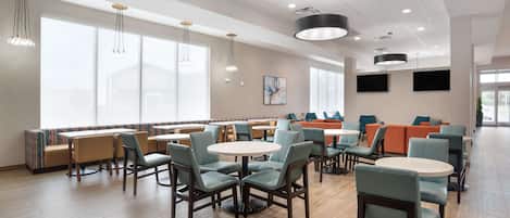 Un comedor moderno con asientos tipo cabina y mesas redondas, ventanas amplias e iluminación suspendida del techo.