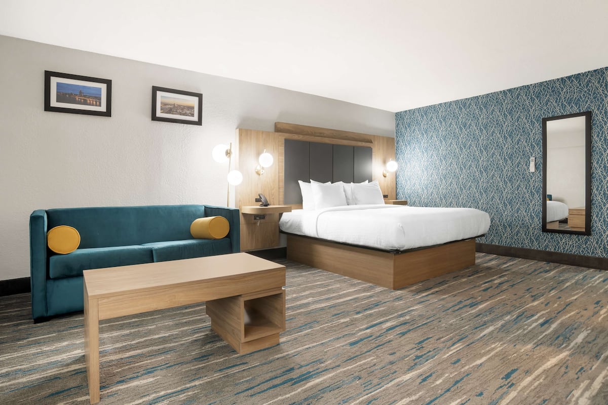 Una habitación de hotel con cama, sofá, mesita de noche, lámparas de pared, cuadros enmarcados y alfombra estampada.