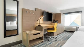 A hotel room with a bed, a desk with a chair, a flat-screen TV, a mirror, and a window with a view.