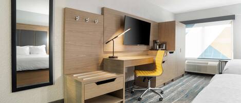 A hotel room with a bed, a desk with a chair, a flat-screen TV, a mirror, and a window with a view.