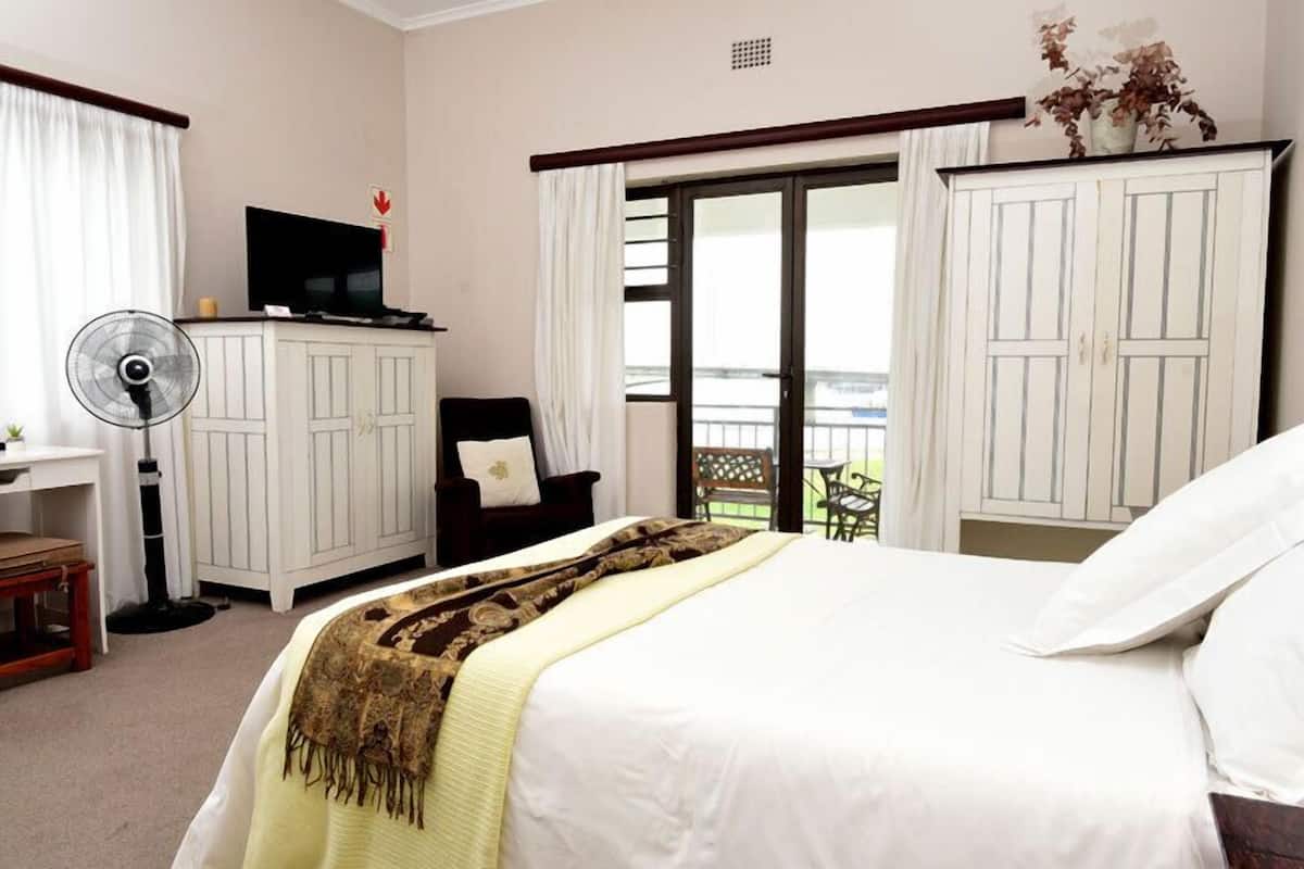 Une chambre d’hôtel avec un lit, un bureau avec un ordinateur, une chaise, un ventilateur et une vue sur l’extérieur.