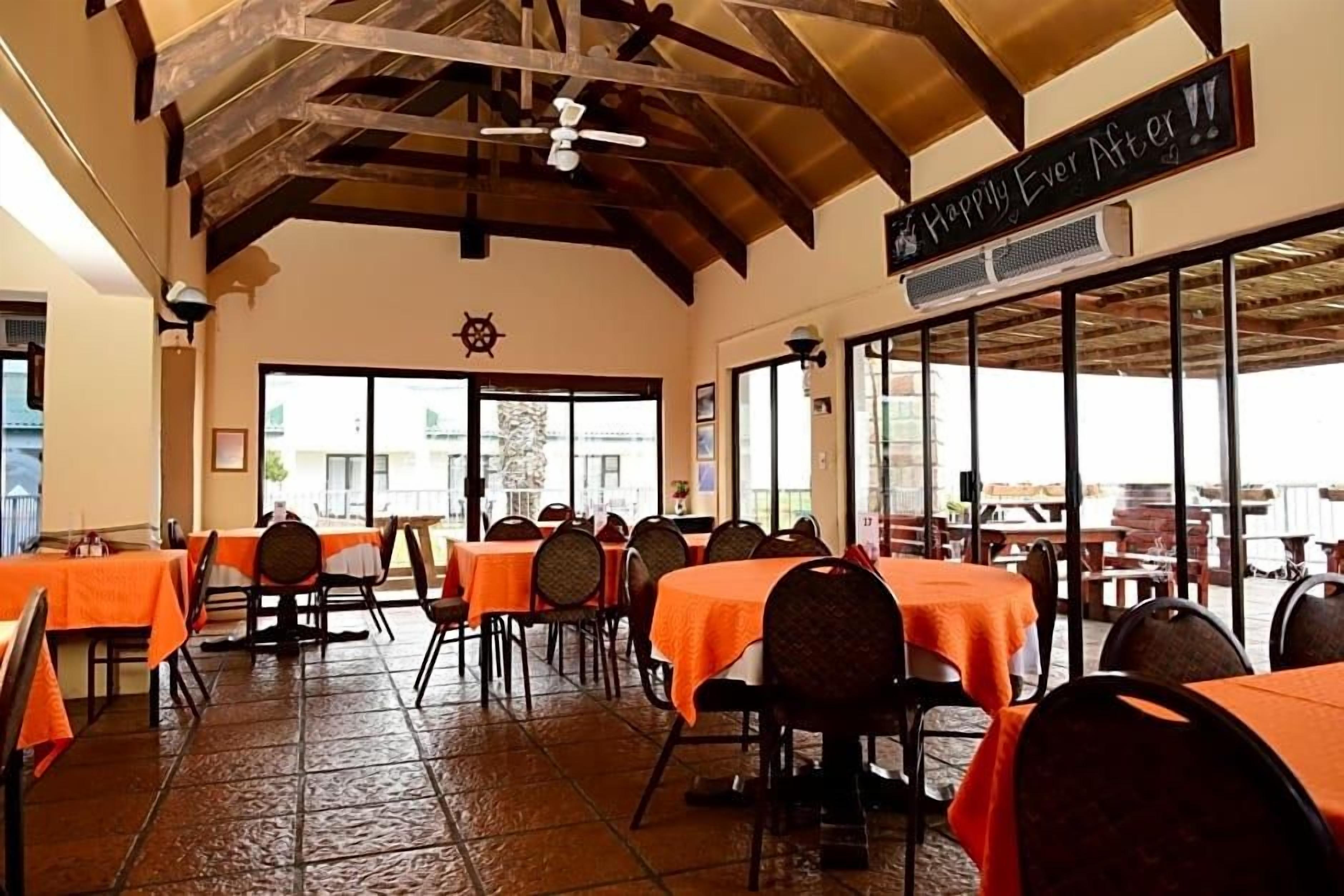 A restaurant with tables covered in orange tablecloths, a ceiling fan, and a sign that reads 'Happy Ever After.'