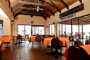 Un restaurante con mesas cubiertas de manteles naranjas, un ventilador de techo y un letrero que dice 'Happy Ever After'.
