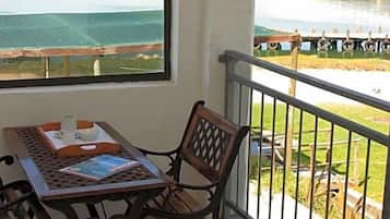 A balcony with a table and chair, a view of a body of water, and a bridge in the distance.