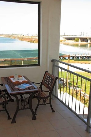 A balcony with a table and chair, a view of a body of water, and a bridge in the distance.