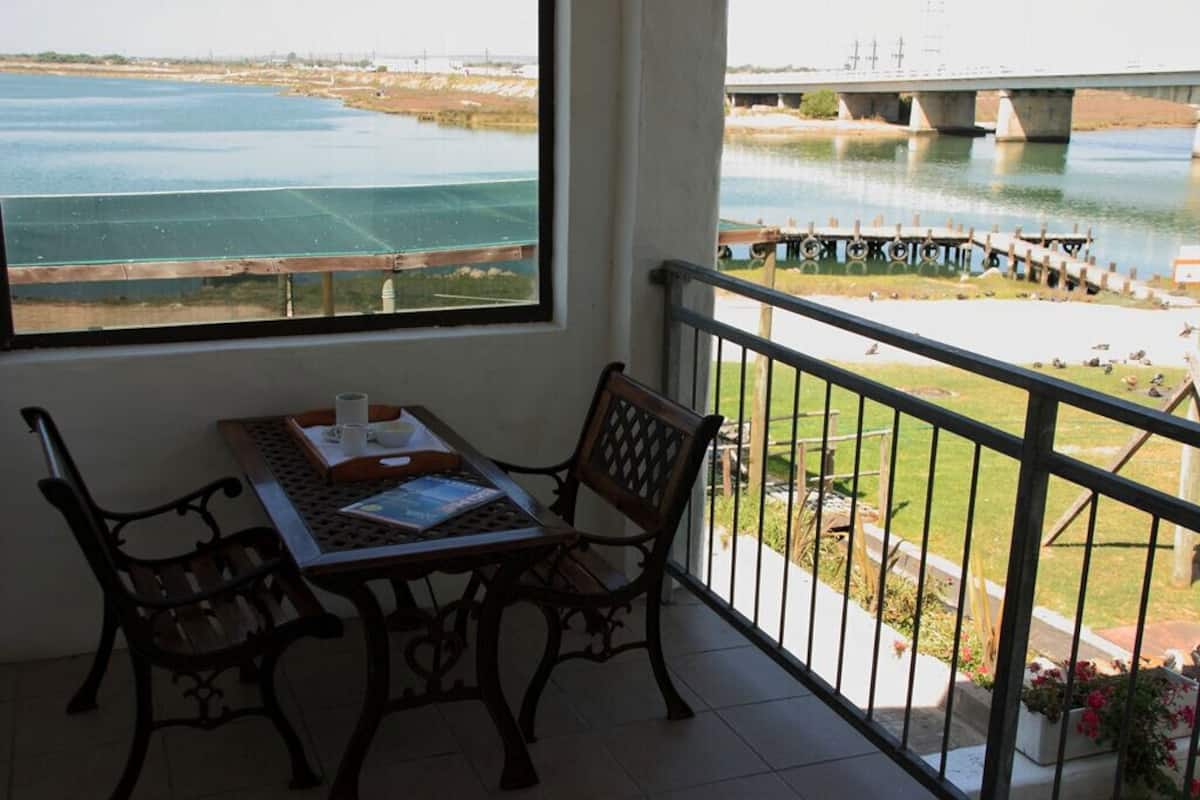 Un balcon avec une table et des chaises, donnant sur une rivière et un pont.