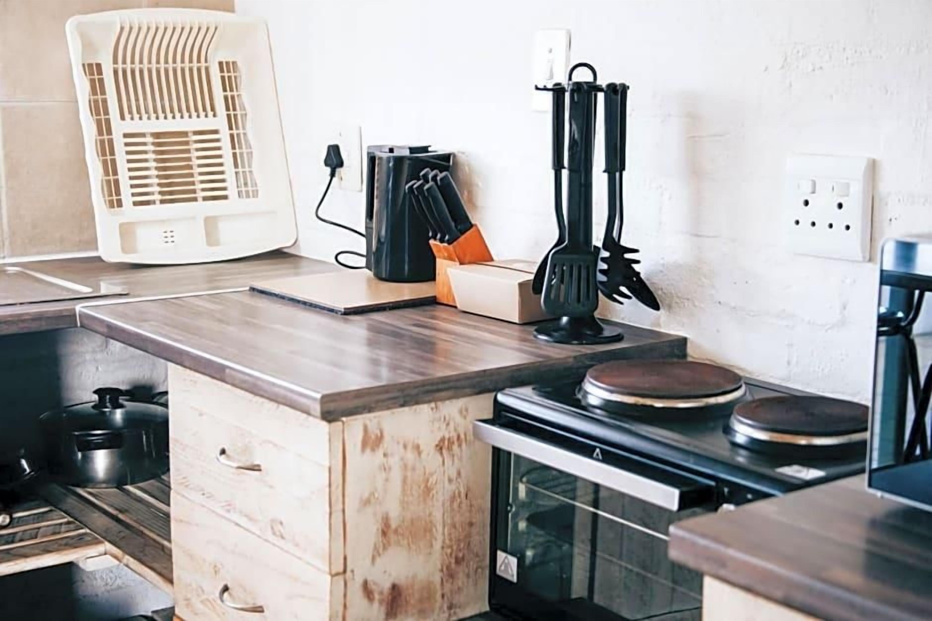 A kitchen with a built-in stove, a white fan, and a set of black utensils on the counter.