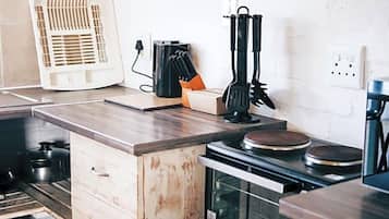 A kitchen with a built-in stove, a white fan, and a set of black utensils on the counter.
