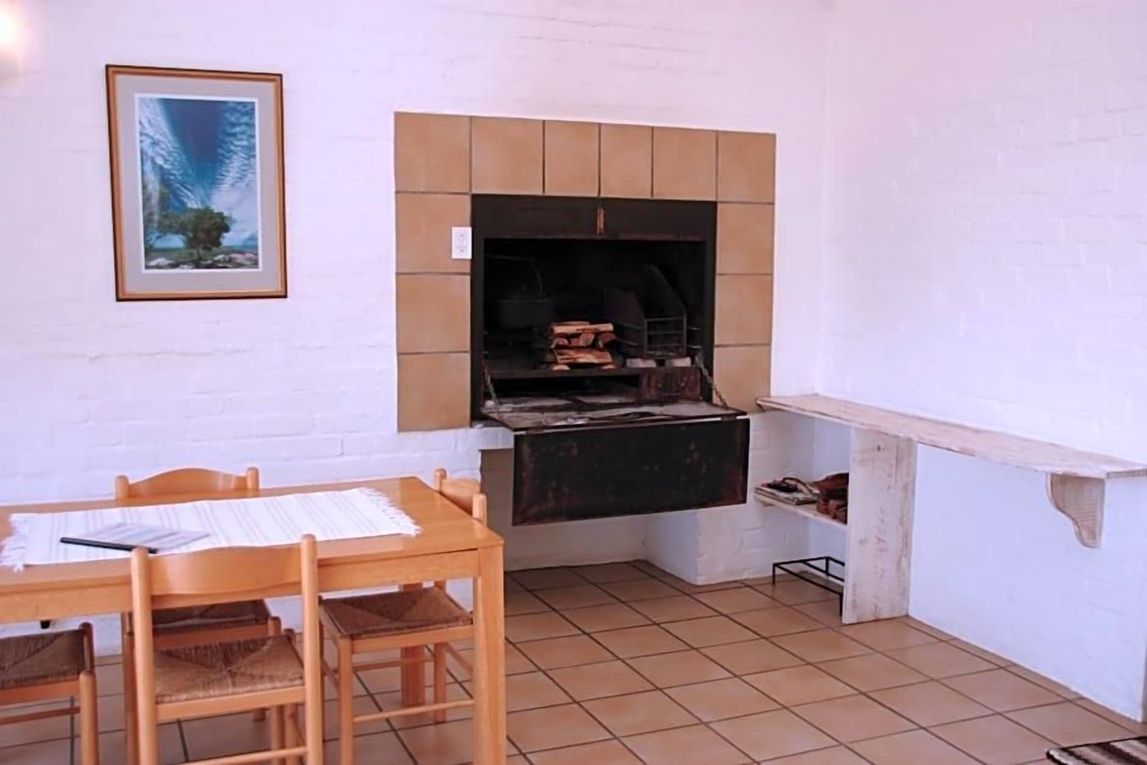 A small kitchen with a tiled floor, a wooden table with chairs, a framed picture on the wall, and a built-in grill.