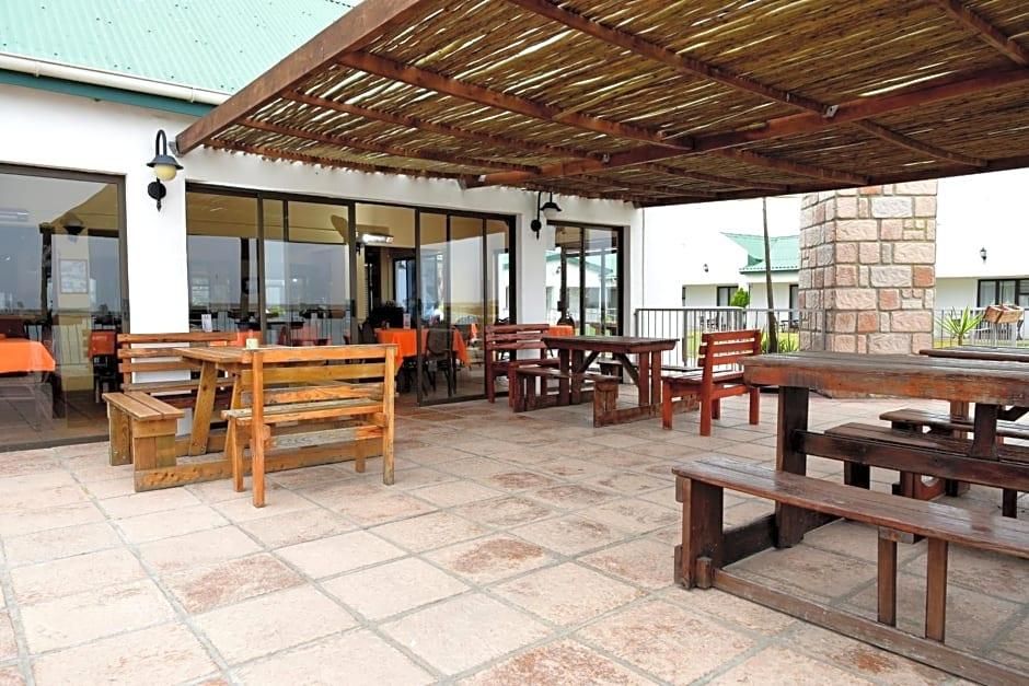 An outdoor patio area with wooden tables and benches, a covered seating area, and a stone pillar.