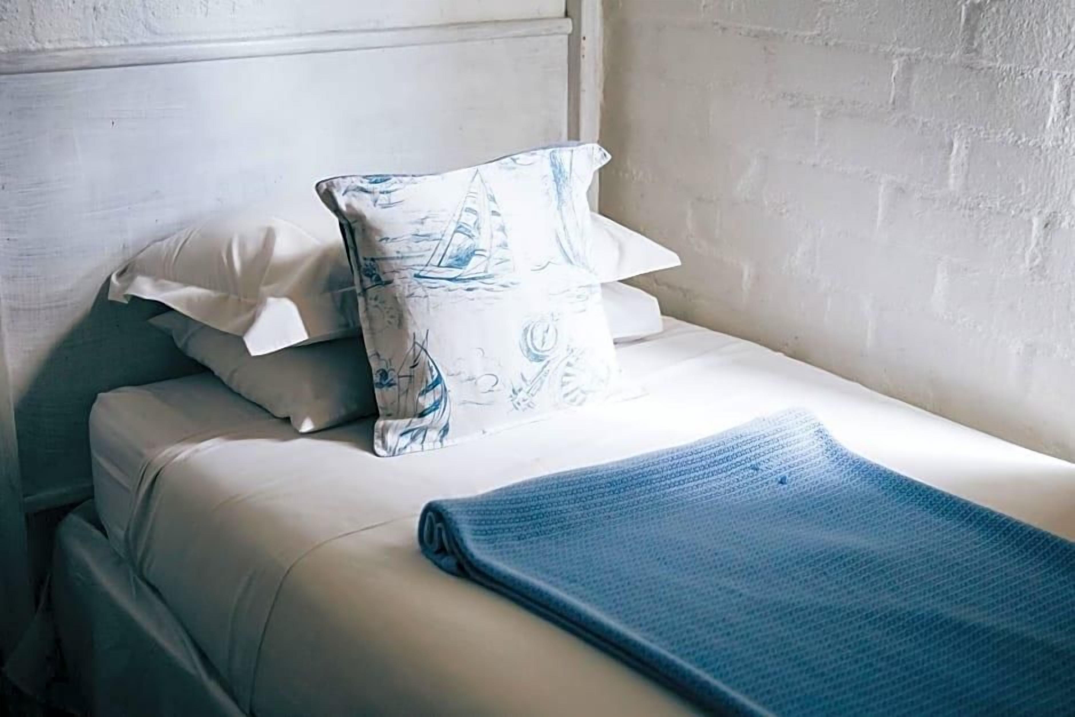Ein Einzelbett mit weißem Kopfteil, einer blauen Decke und gemusterten Kissen.