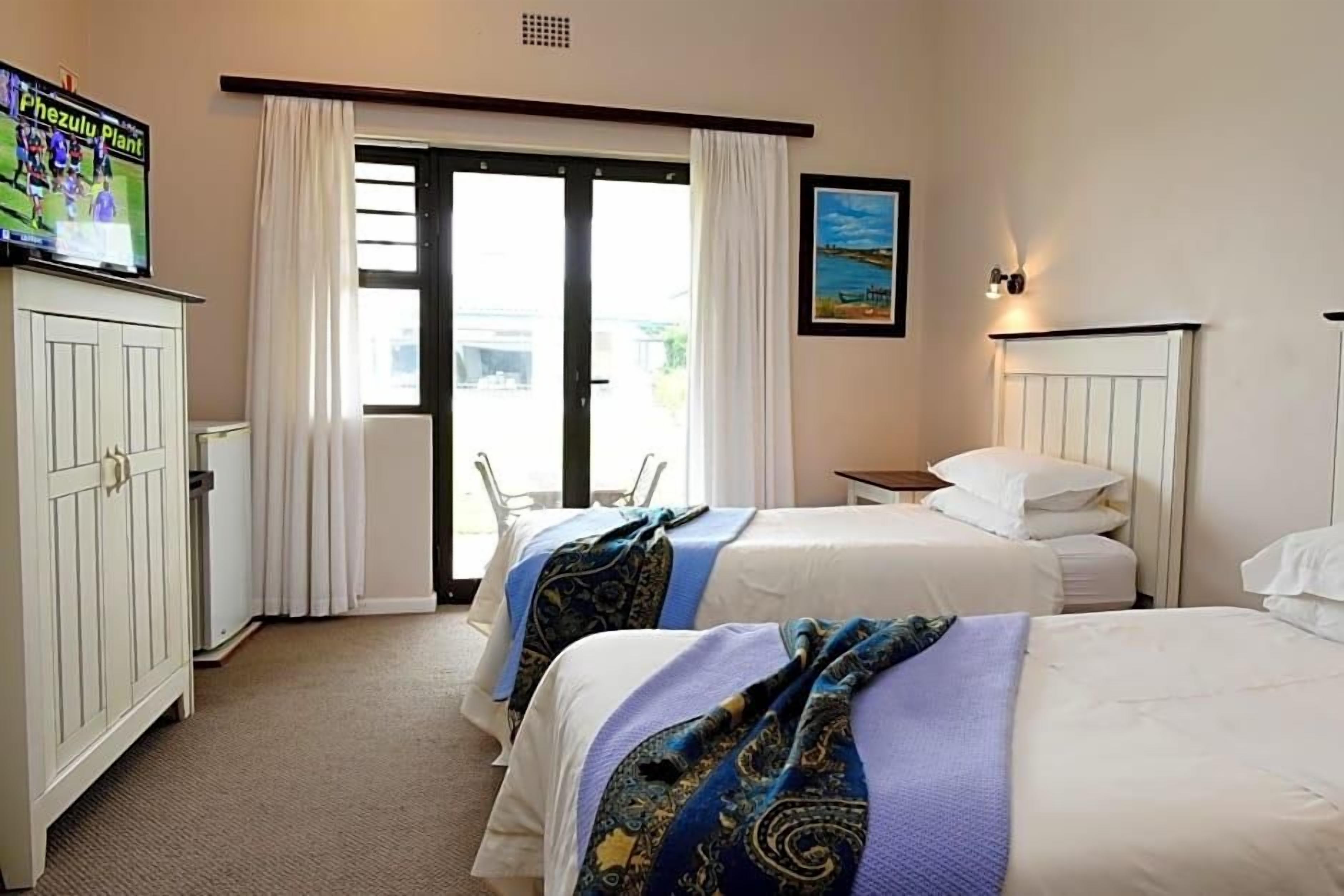A hotel room with two beds, a television, a painting, and a view through the door.