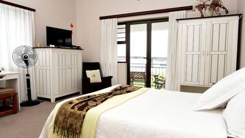 Habitación de hotel con cama, escritorio con computadora, silla, ventilador y vista al exterior.