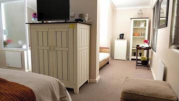 A bedroom with a bed, a wardrobe, a television, a small table with a kettle, and a window.