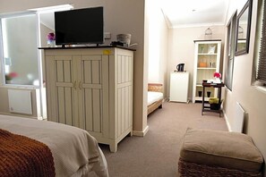 Une chambre à coucher comprenant un lit, une armoire, une télévision, une petite table avec une bouilloire et une fenêtre.