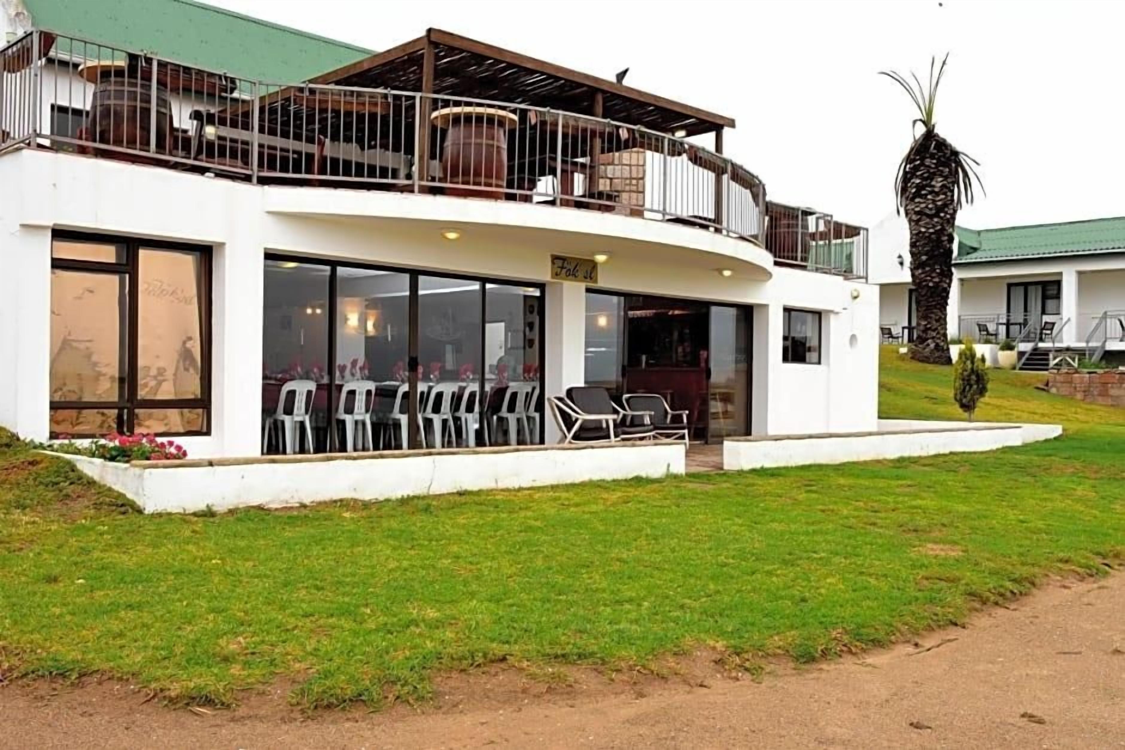 A two-story building with a balcony, outdoor seating, and a palm tree.