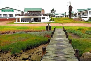 A wooden pathway leading to a hotel with a green roof and a sign that reads 'RIVIERA HOTEL Die Pont Restaurant.' - Riviera Hotel (Bergrivier)