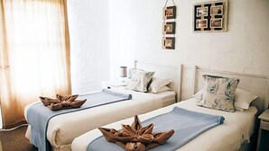 A hotel room with two beds, each with a towel art centerpiece, a bedside table with a lamp, and a wall-mounted photo frame. - Riviera Hotel (Bergrivier)