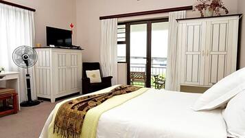 Habitación de hotel con cama, escritorio, silla, televisor, ventilador y vista al exterior.