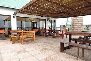 An outdoor patio area with wooden tables and benches, a covered seating area, and a stone pillar.