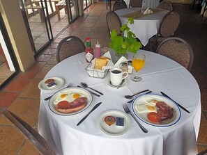 A breakfast table with plates of eggs, bacon, and toast, a glass of orange juice, and condiments. - Riviera Hotel (Bergrivier)